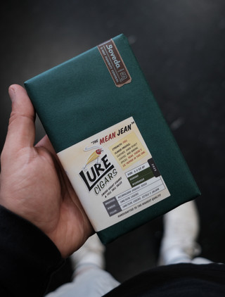 Hand holding a green box of 'Lure Cigars' with a label on a dark background