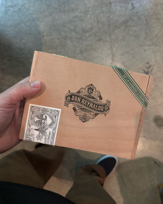 Hand holding a wooden box with 'Don Reynaldo' branding on a textured surface