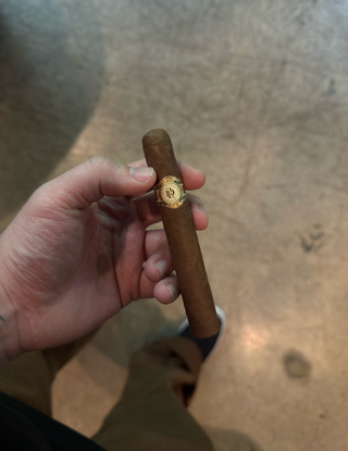 Hand holding a cigar with a visible brand logo against a wooden background